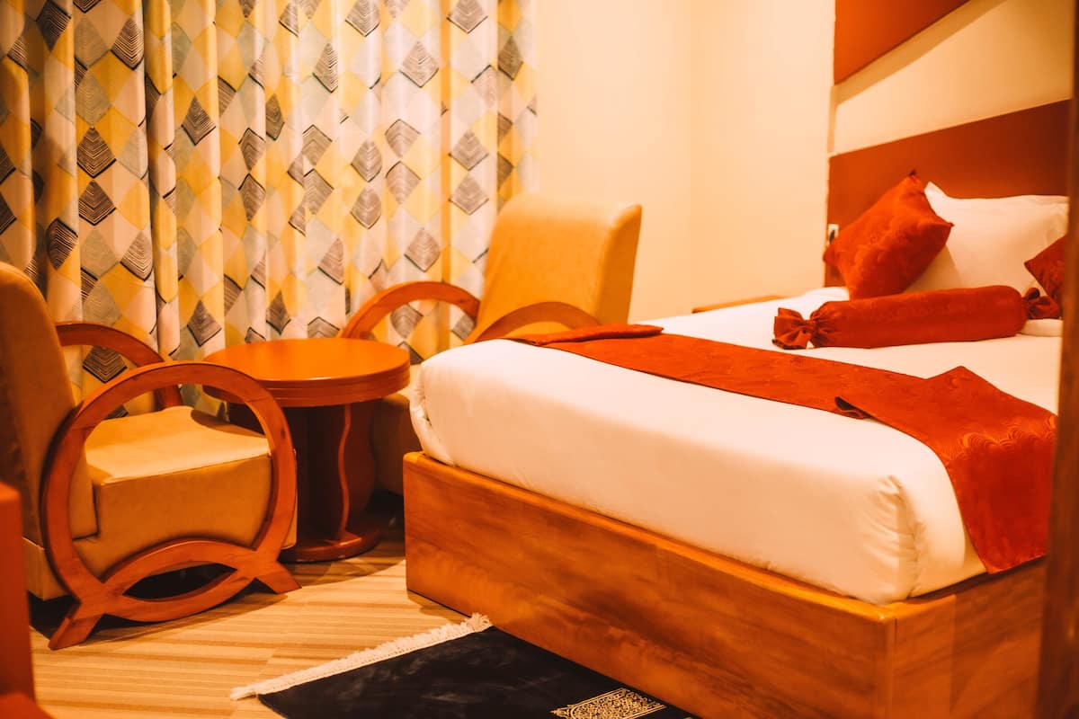 Una habitación de hotel con una cama de madera, una mesita redonda pequeña y dos sillas de madera.