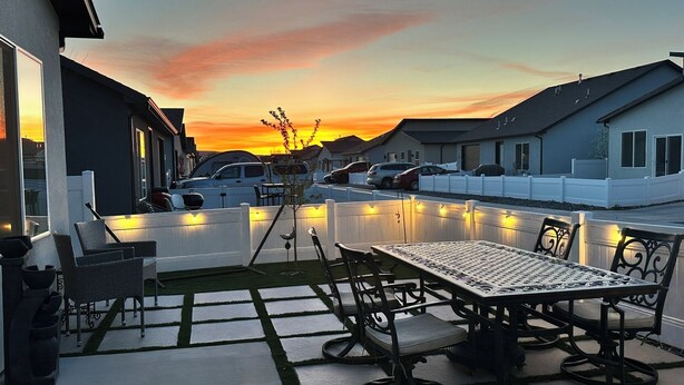Un patio exterior con una mesa y sillas, una valla blanca y una puesta de sol al fondo.