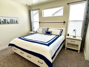 Un dormitorio ordenado con una cama grande, mesitas de noche, un escritorio y una ventana con cortinas.