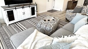 Una sala de estar con un televisor de pantalla plana grande, un mueble blanco con tiradores negros, alfombras estampadas y un sofá con cojines.