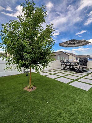 Un patio con mesa y sillas, un árbol y cielo despejado.