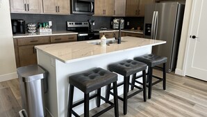 Una cocina moderna con armarios de madera, un refrigerador de acero inoxidable, un microondas y una barra para café.