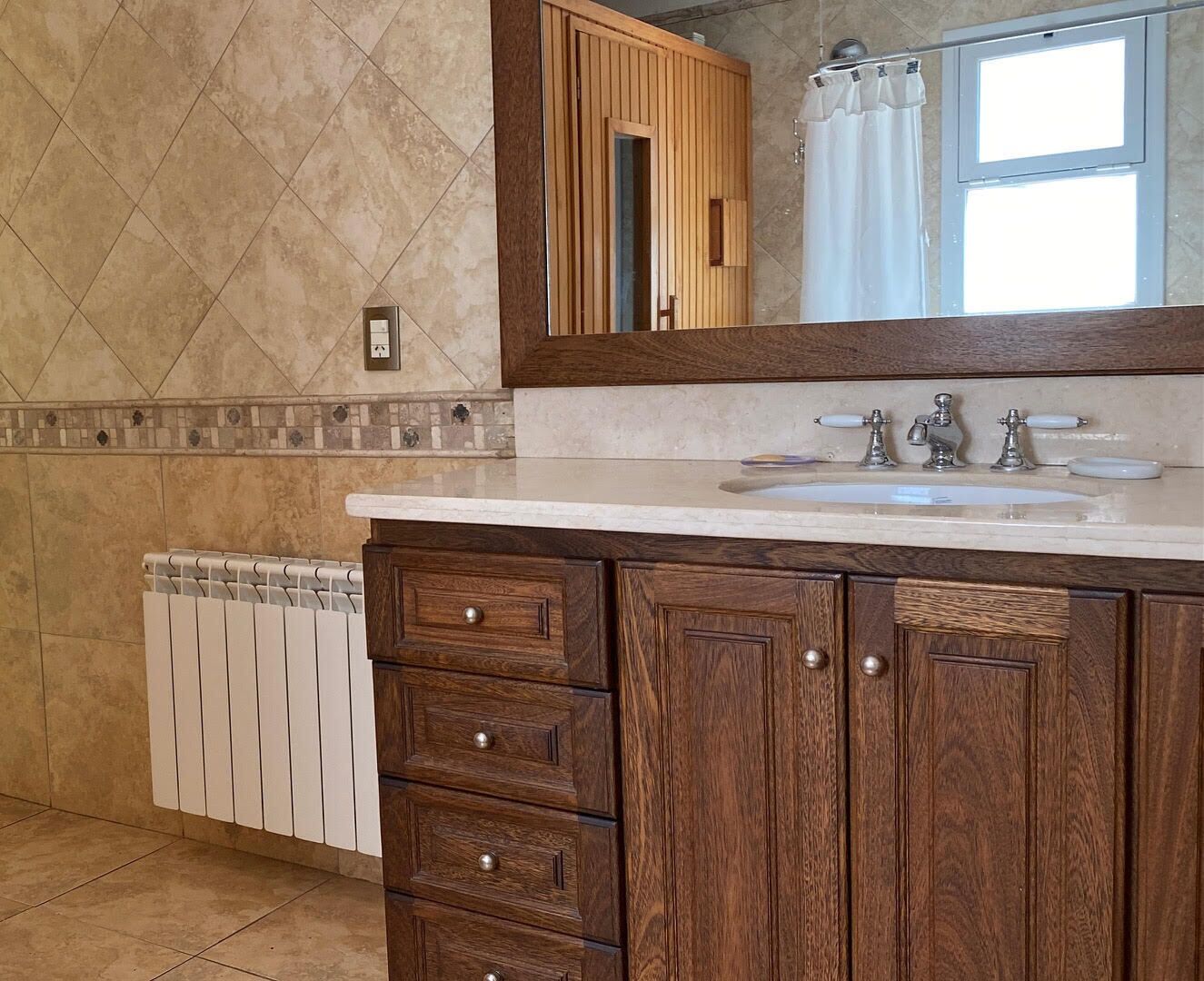A bathroom with a wooden vanity, a white sink, and a mirror above it.