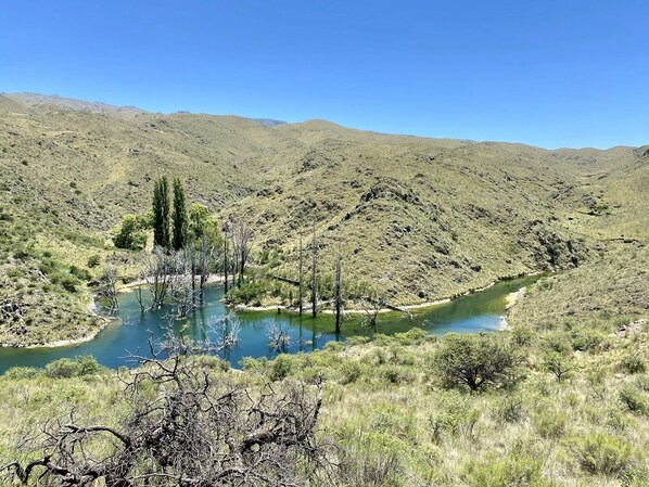 Un paisaje natural con un río, colinas y vegetación escasa.