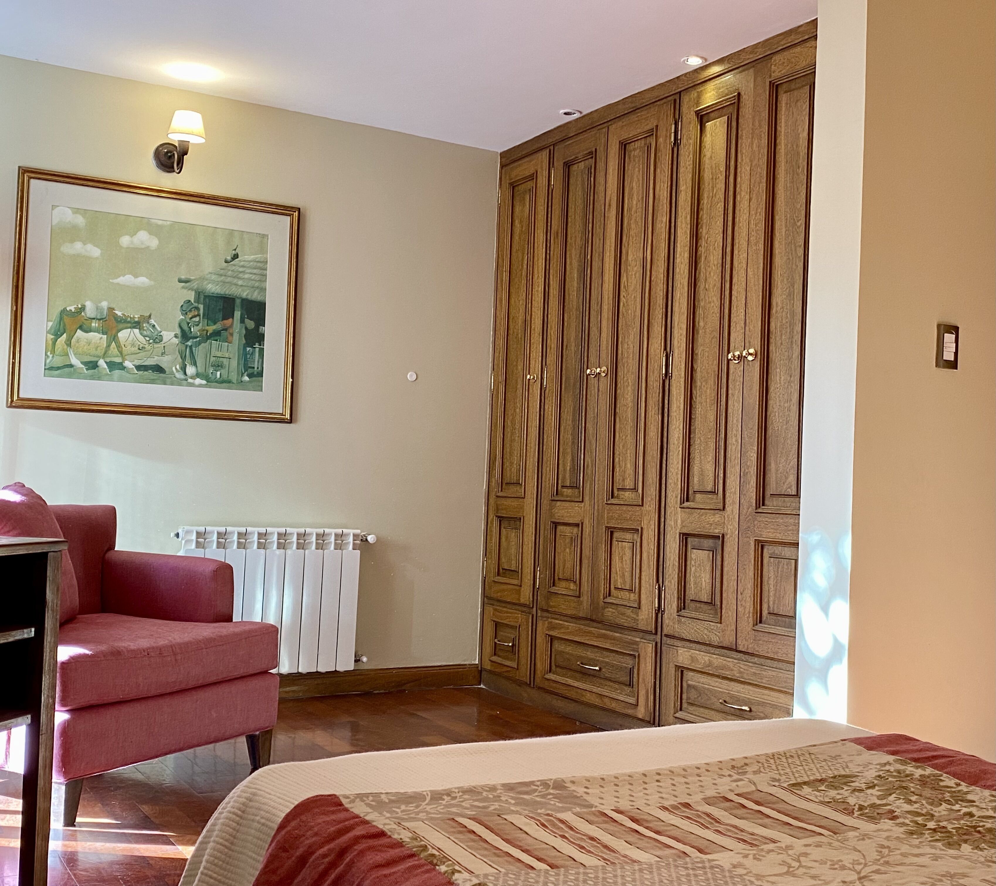 A bedroom with a large wardrobe, a framed picture on the wall, a radiator, and a red chair.