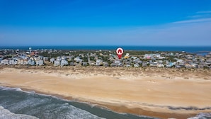 Luftaufnahme einer Küstenstadt mit Strand im Vordergrund und einem dichten Häuserensemble im Hintergrund.