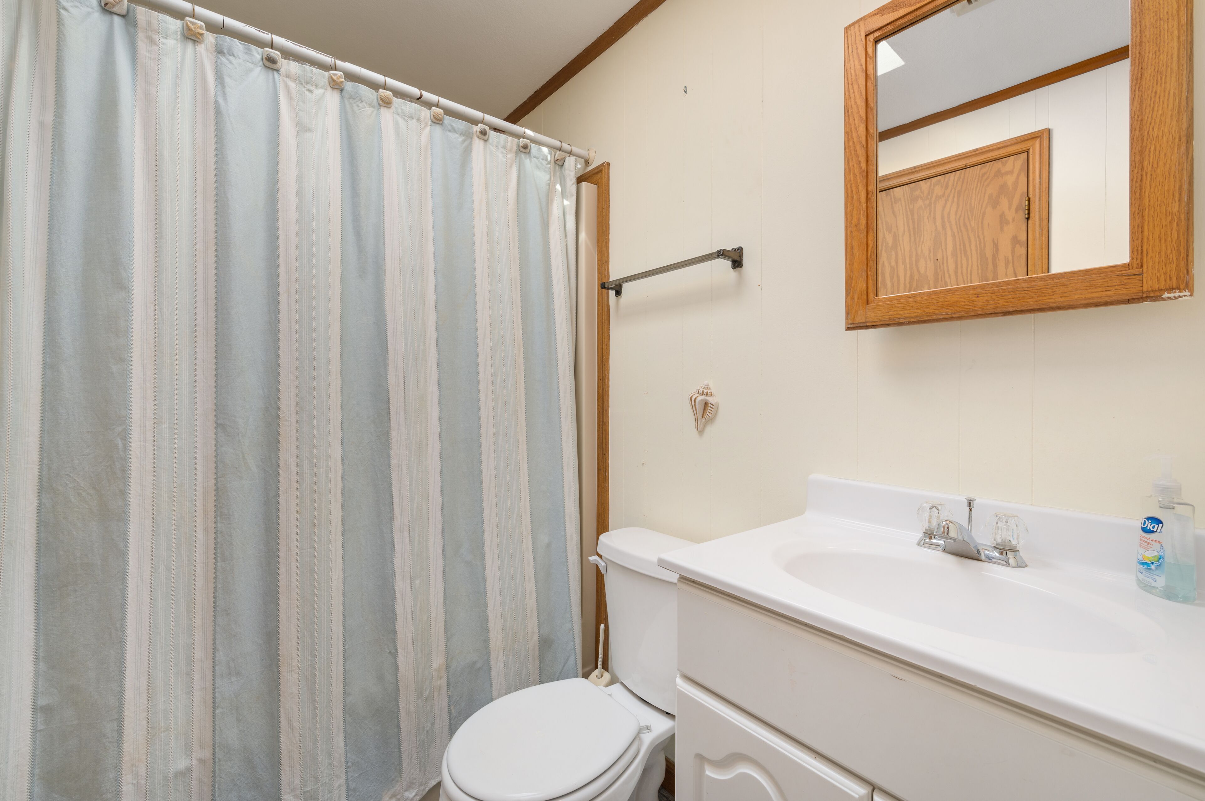 A bathroom with a striped shower curtain, a wooden medicine cabinet, a toilet, and a sink with a soap dispenser.
