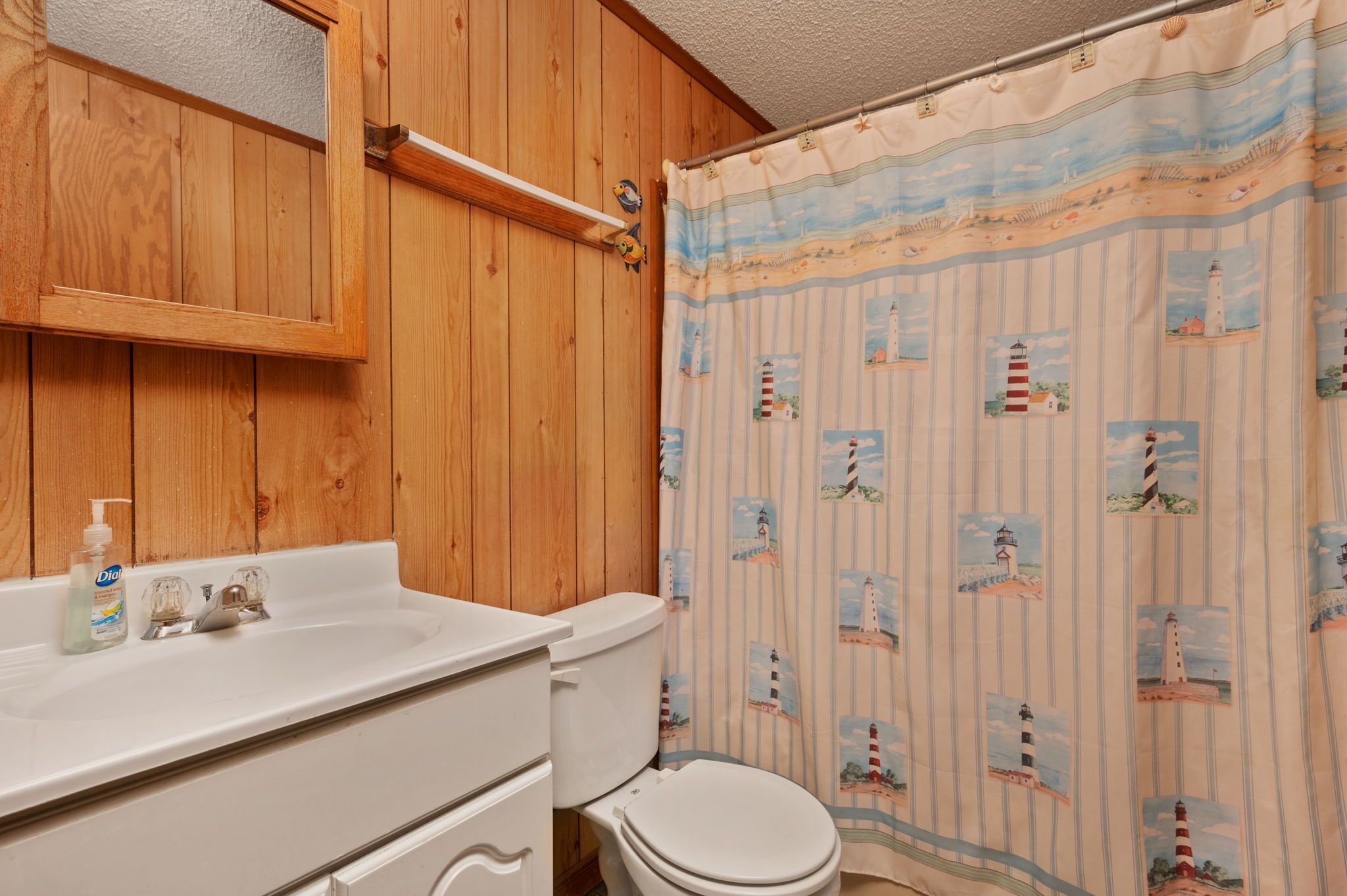 Een badkamer met houten wanden, een witte wastafel, een toilet en een douchegordijn met afbeeldingen van vuurtorens.