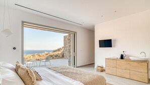 Quarto com uma cama grande, cômoda de madeira, televisão e vista para o mar.