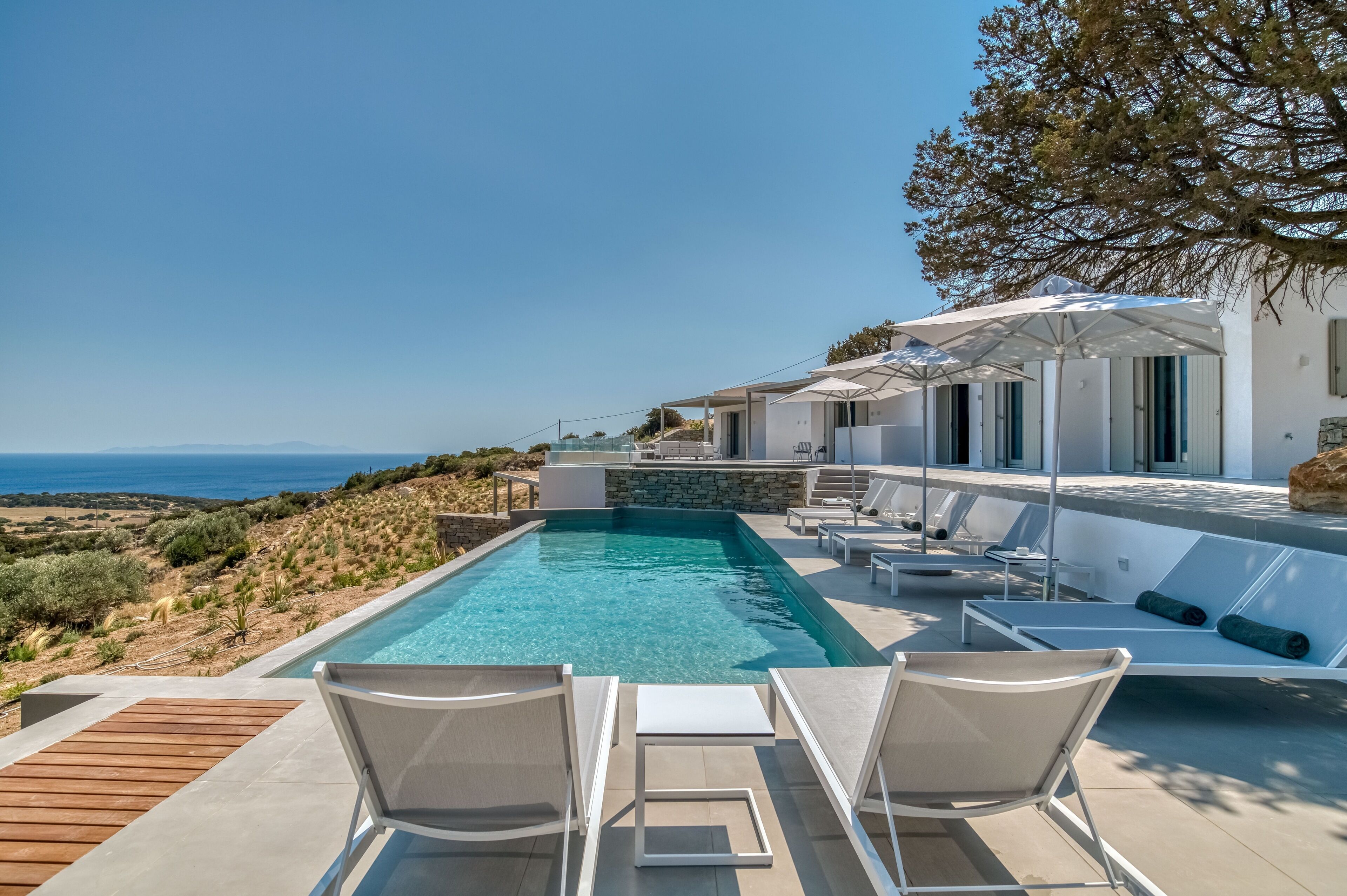 A modern pool area with lounge chairs and umbrellas, overlooking a scenic landscape.