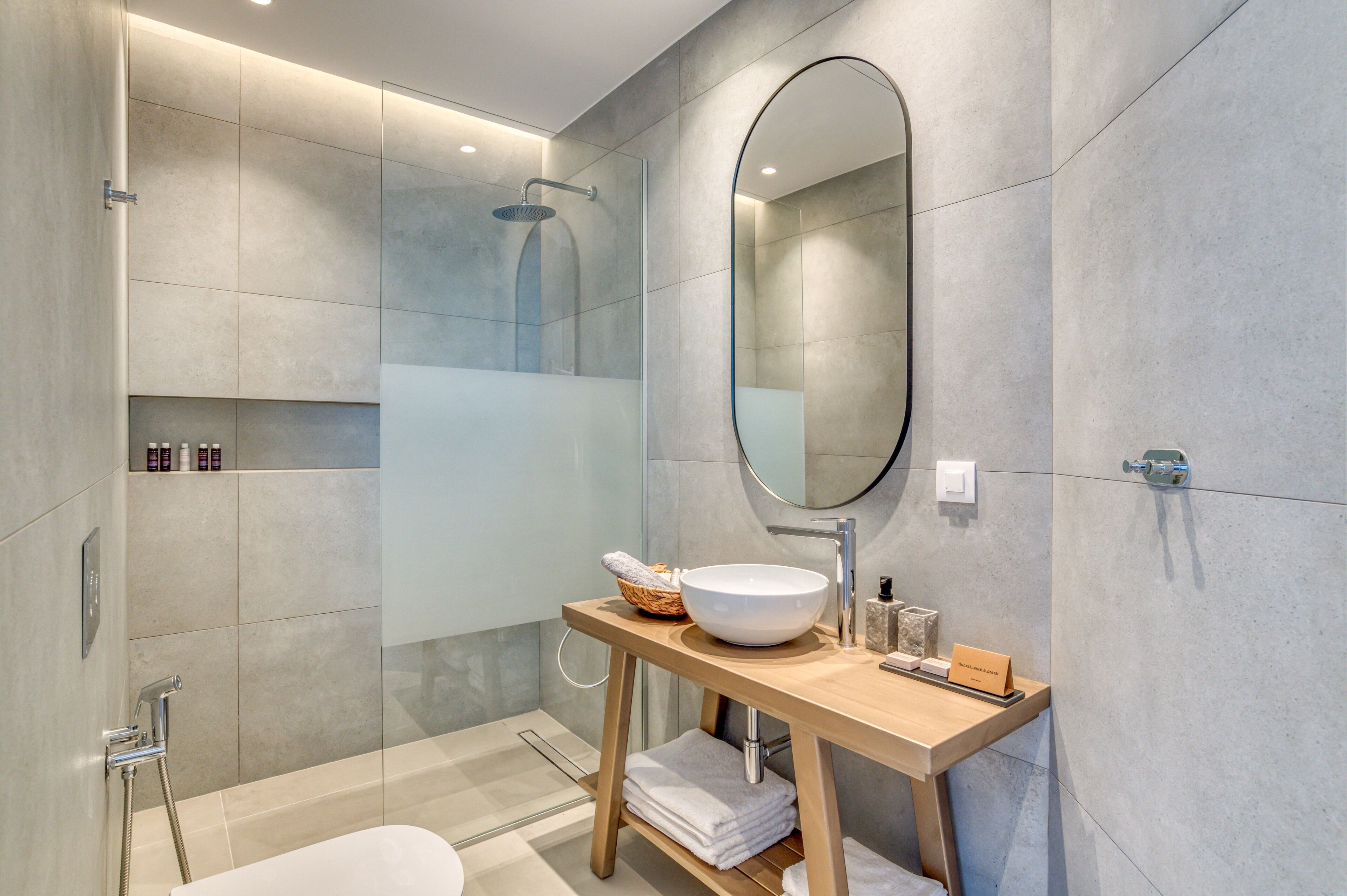 Un bagno moderno con doccia vetrata, un mobile contenitore in legno con uno specchio grande e un lavandino bianco.