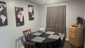 A dining area with a round table, wooden chairs, a coffee maker, and a cabinet.