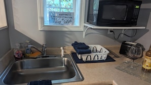 A kitchen with a stainless steel sink, a black microwave, a toaster, and a bottle of vanilla syrup.