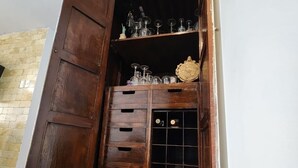 A room with a wooden cabinet containing glassware and a decorative plate. A black horse statue is on a round wooden table.