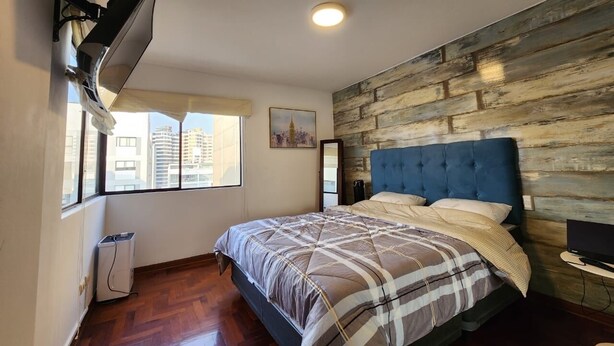 A bedroom with a bed, a TV, a window, and a wall-mounted heater.