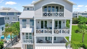 A two-story house with a balcony on the upper floor, a pool in the backyard, and a well-maintained lawn. - Seahorse Villa! Amazing Ocean Views, Heated Pool, Private Elevator, Steps to Beach (Saint Simons Island)