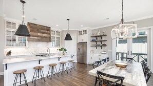 A modern kitchen with a central island, bar stools, a large dining table, and a refrigerator. - Seahorse Villa! Amazing Ocean Views, Heated Pool, Private Elevator, Steps to Beach (Saint Simons Island)