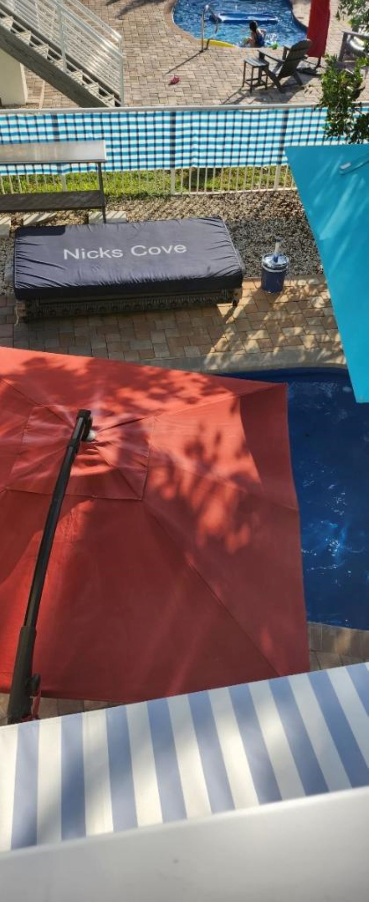 A pool area with a red mat, a blue checkered tablecloth, and a black lounge chair labeled "Nicks Cove".