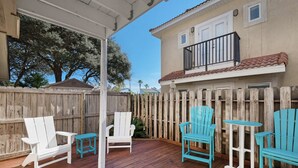 An outdoor patio with wooden deck, white and blue Adirondack chairs, and a small round table.