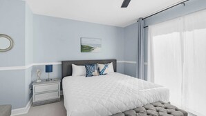 A bedroom with a large bed, a nightstand, a lamp, a chair, and a window with curtains.
