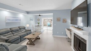 A living room with a sofa, coffee table, and TV. There is a dining area with a table and chairs.