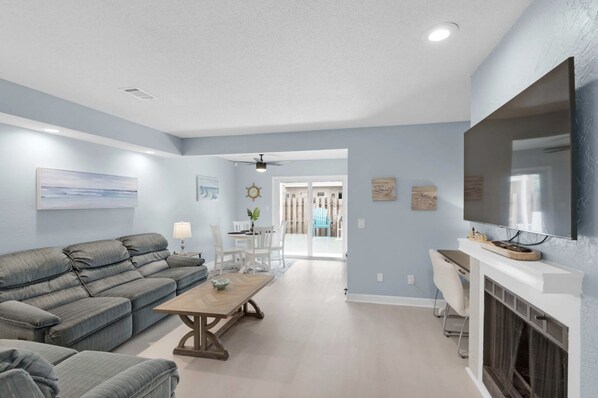 A living room with a sofa, coffee table, and TV. There is a dining area with a table and chairs.