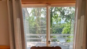 A dining table with a glass centerpiece containing decorative items, a wooden chair in the background, and a view of a deck and greenery outside. - Lakeview Cottage (Ballston Lake)