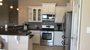 A modern kitchen with white cabinets, stainless steel appliances, and a black countertop. - Single Family Home - 52 BP (Laguna Vista)