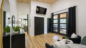 A modern living room with a flat-screen TV, black and white furniture, and a large sliding glass door to the outdoors.