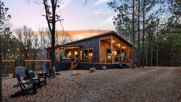 A cabin with a wooden deck, a fire pit, and a covered outdoor seating area.