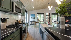 A modern kitchen with a central island, stainless steel appliances, and a wooden ceiling.
