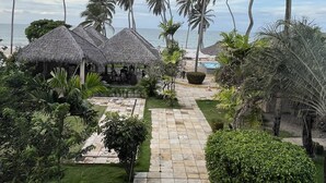 A pathway leading to a beachside area with thatched umbrellas and palm trees. - Eco Paradise - Hospedagem pé na Areia (Praia de Cumbuco Caucaia)