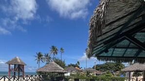 A clear blue swimming pool with lounge chairs and umbrellas, surrounded by palm trees and a thatched-roof structure. - Eco Paradise - Hospedagem pé na Areia (Praia de Cumbuco Caucaia)