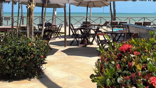 A beachside resort with palm trees, outdoor seating, and a view of the ocean. - Eco Paradise - Hospedagem pé na Areia (Praia de Cumbuco Caucaia)