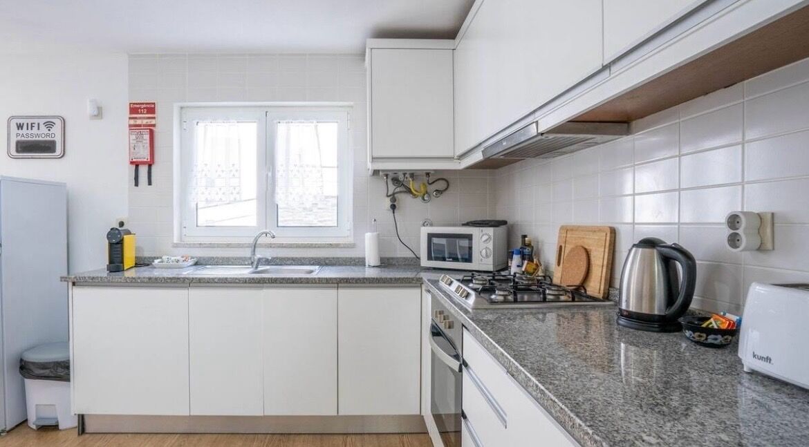 Une cuisine compacte avec des meubles blancs, un plan de travail en granit, un four à micro-ondes, une bouilloire et un grille-pain.