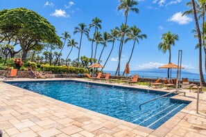 A swimming pool with lounge chairs and umbrellas, surrounded by palm trees and a view of the ocean. - Luxurious Oceanfront Condo at Wailea Elua Village - Unit 1201, Central AC, Wi-Fi (Kihei)