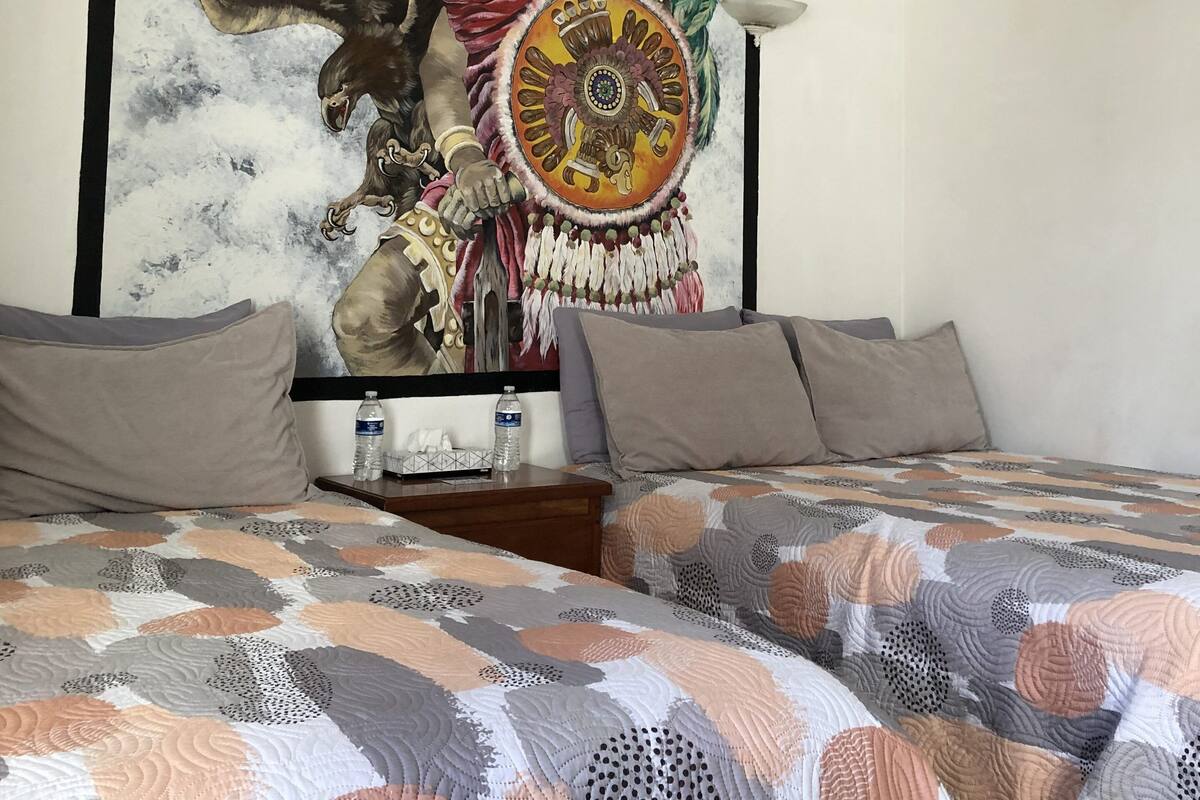 A bedroom with a large mural of an eagle and a circular emblem, a bed with a patterned quilt, and a bedside table with a water bottle.
