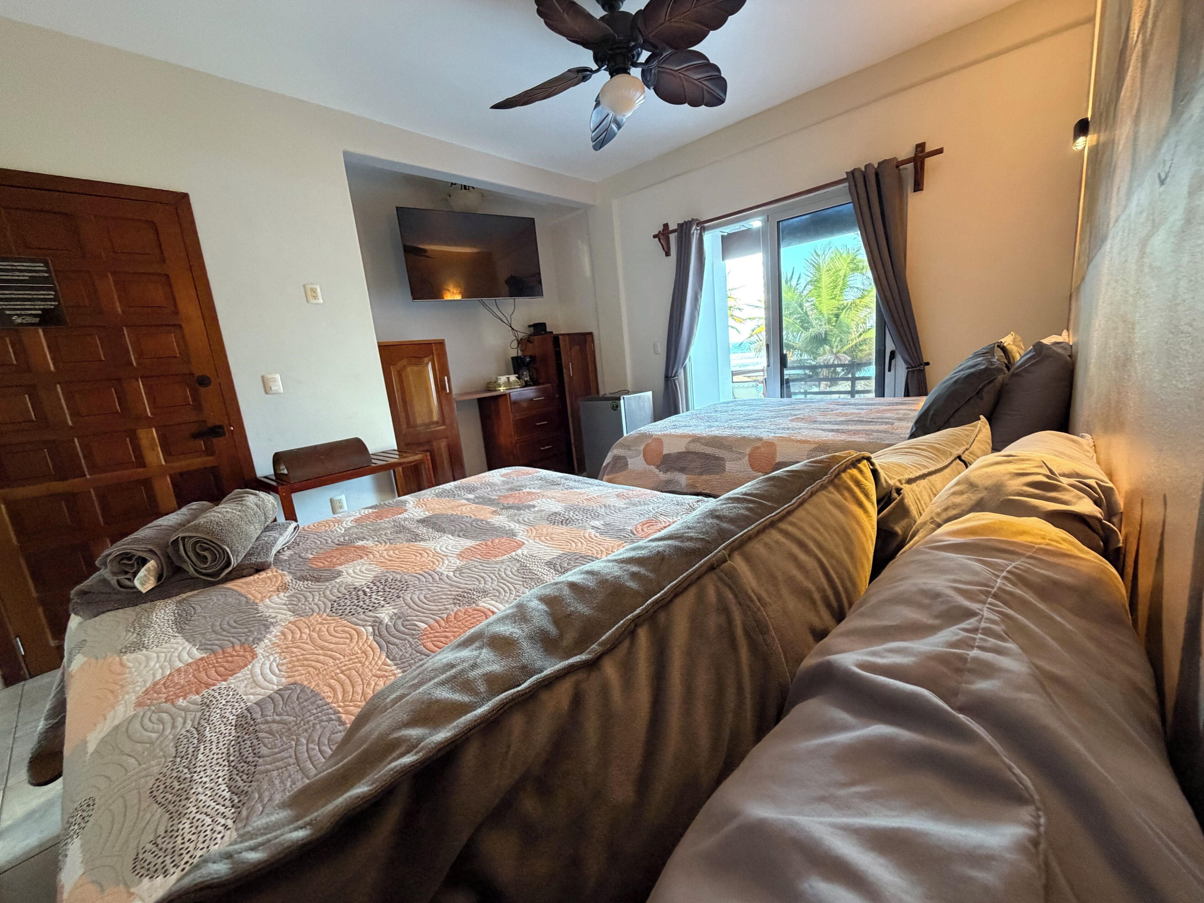 A bedroom with two beds, a ceiling fan, a TV, a desk, and a window with curtains.