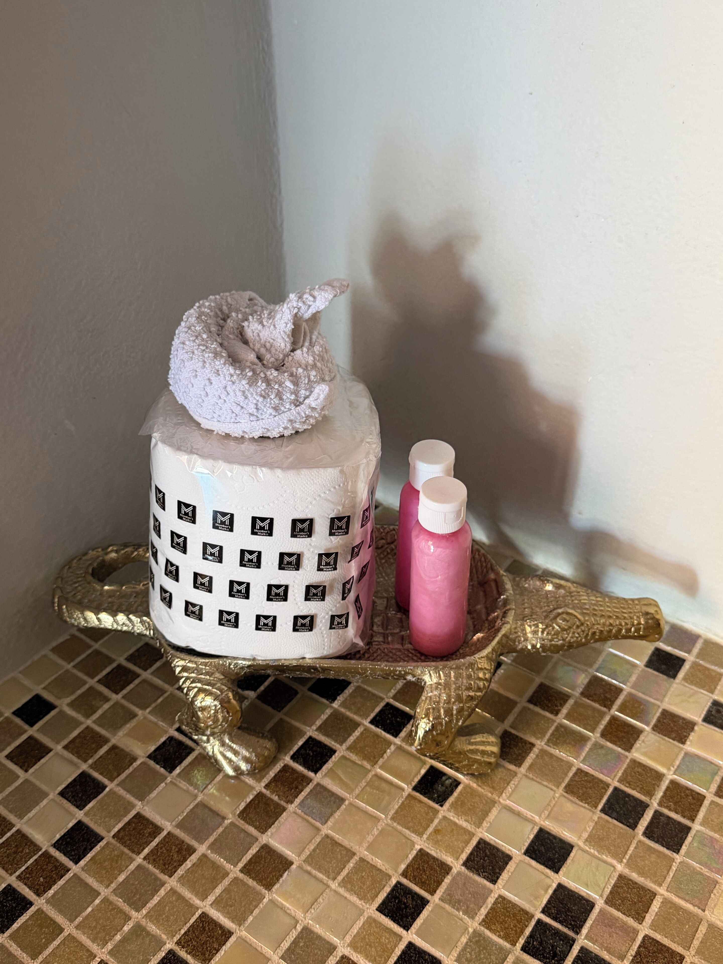 Un tocador de baño con una toalla blanca, una botella rosa y una bandeja dorada.