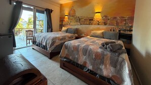 A hotel room with two beds, a ceiling fan, a mural, and a view of the outdoors. - Hotel El Caballo Blanco (Mahahual)