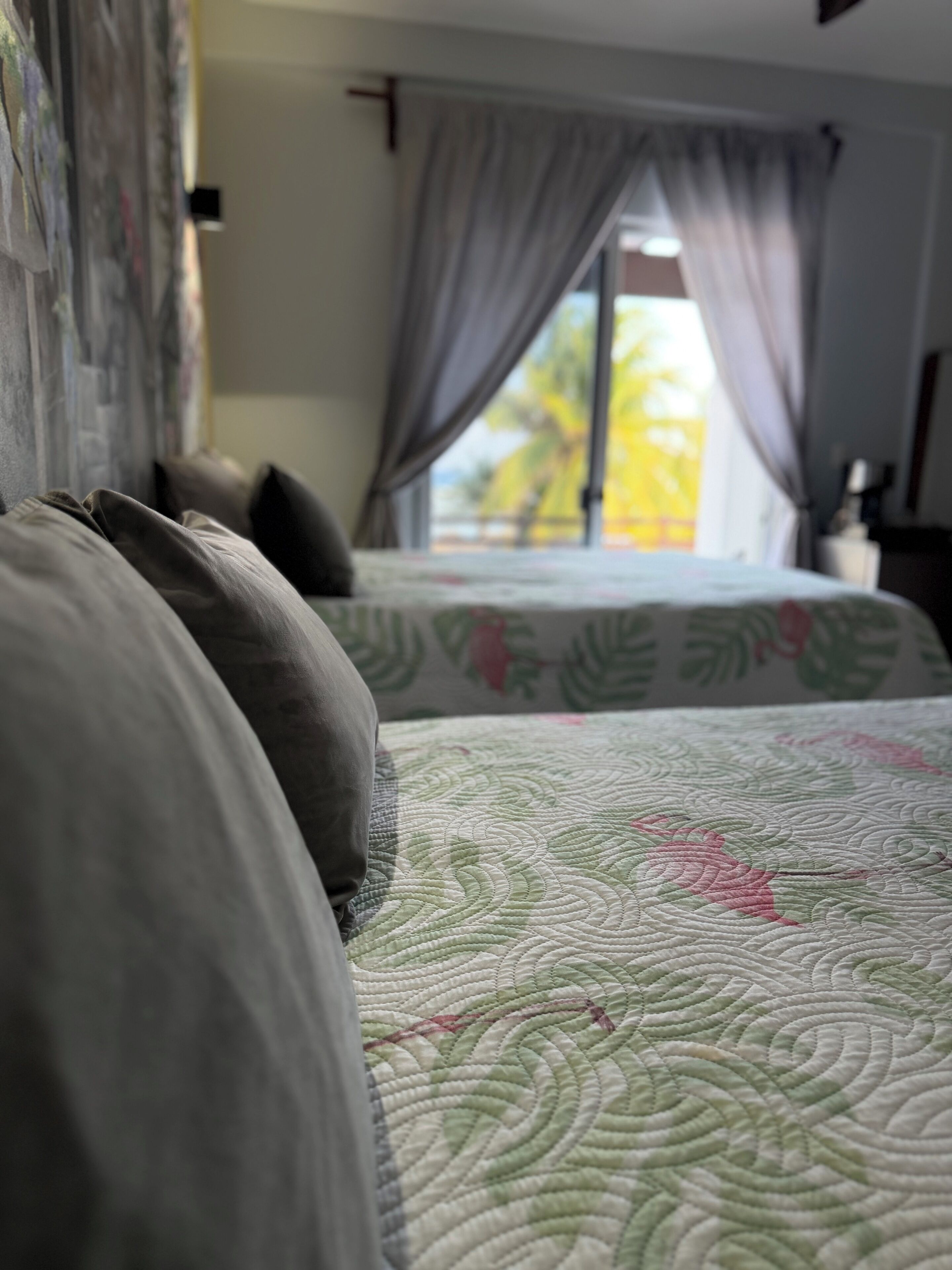 Una cama con colcha estampada, una ventana con cortinas y vista a árboles.
