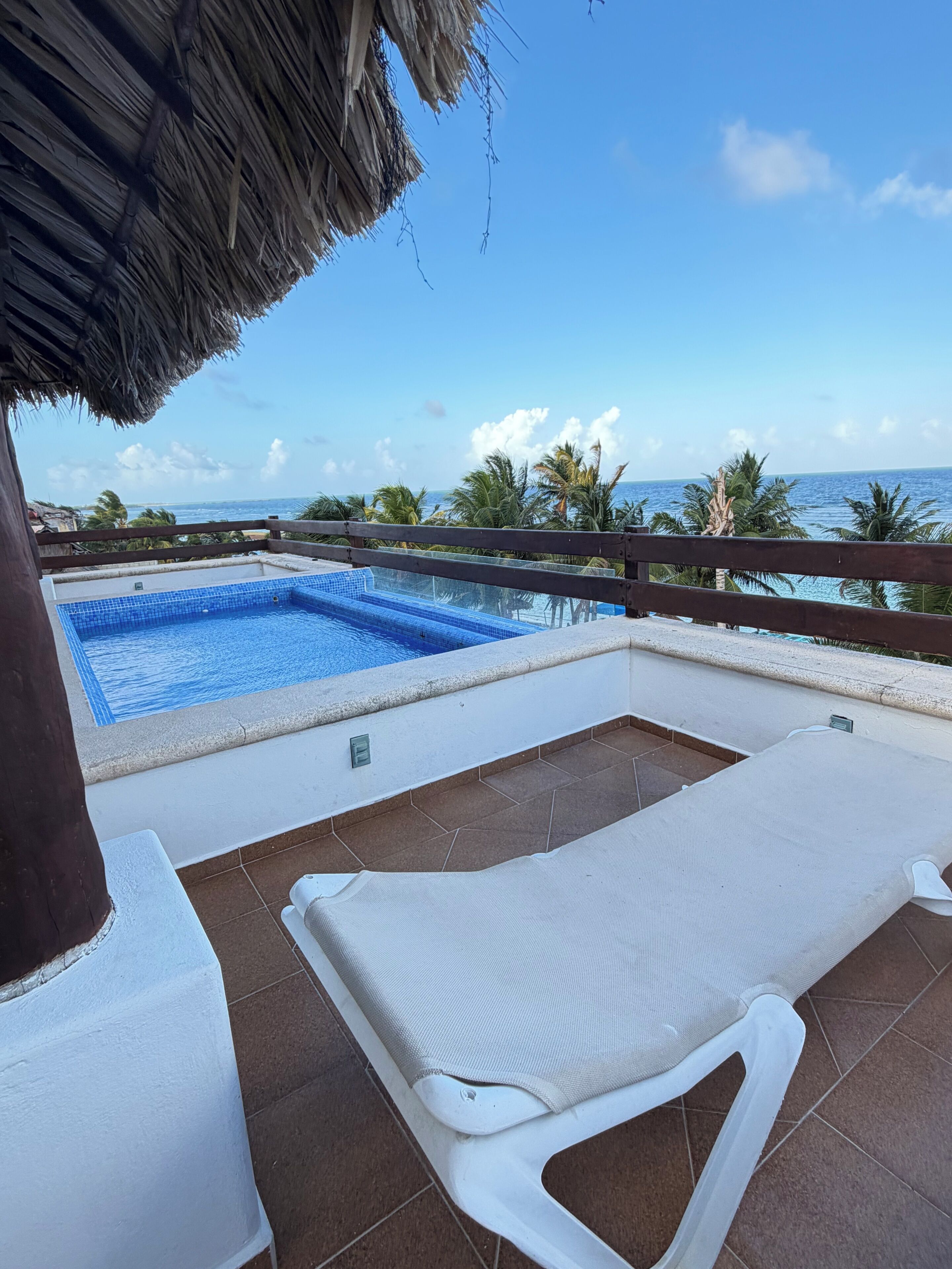 A pool with clear blue water, a white lounge chair, and a view of the ocean.