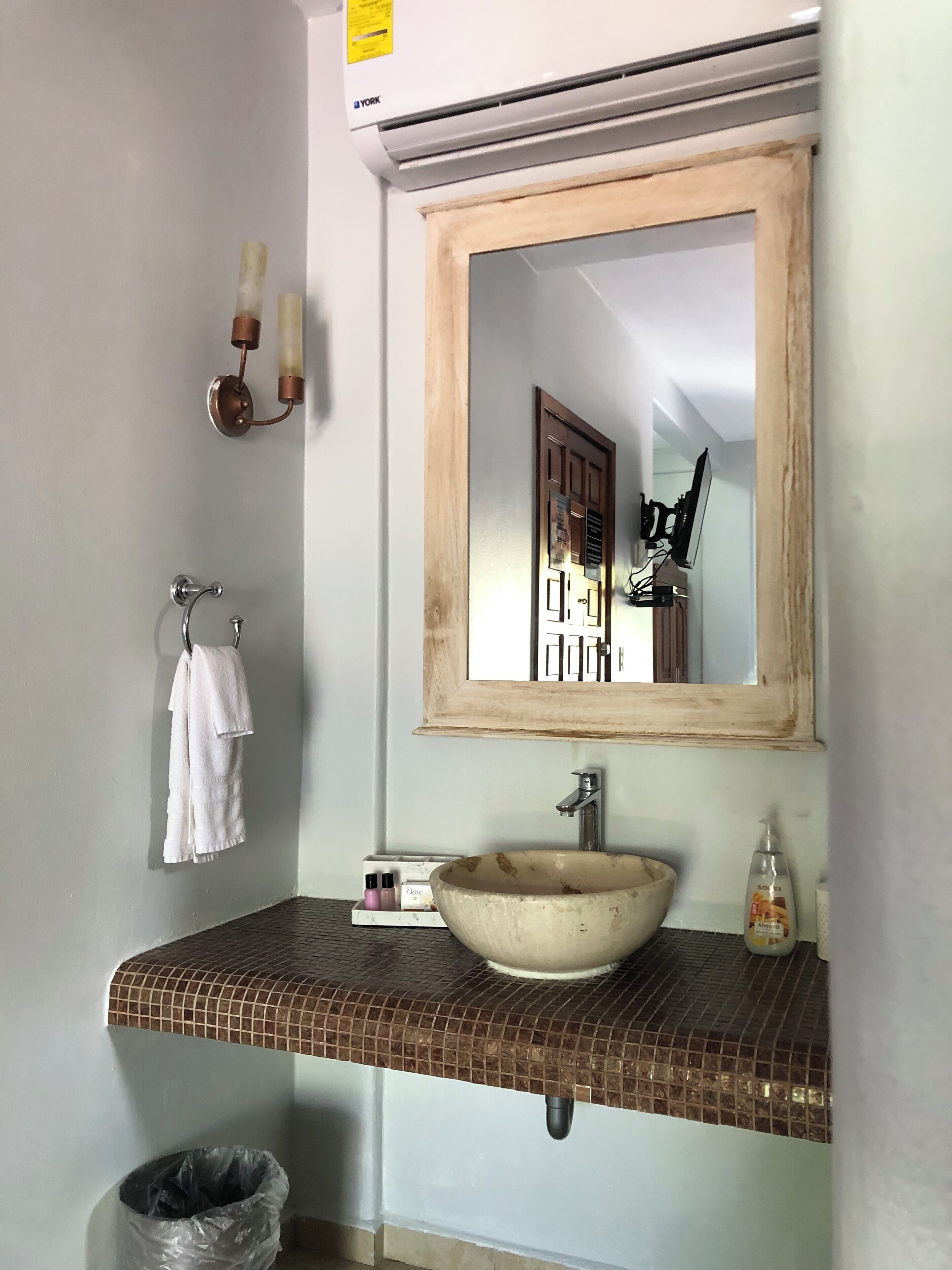 A bathroom with a tiled sink, a mirror, a towel rack, and a trash can.