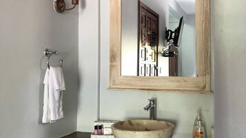 A bathroom with a tiled sink, a mirror, a towel rack, and a trash can.