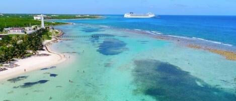 Una zona costera con playa, muelle y un crucero en la distancia.