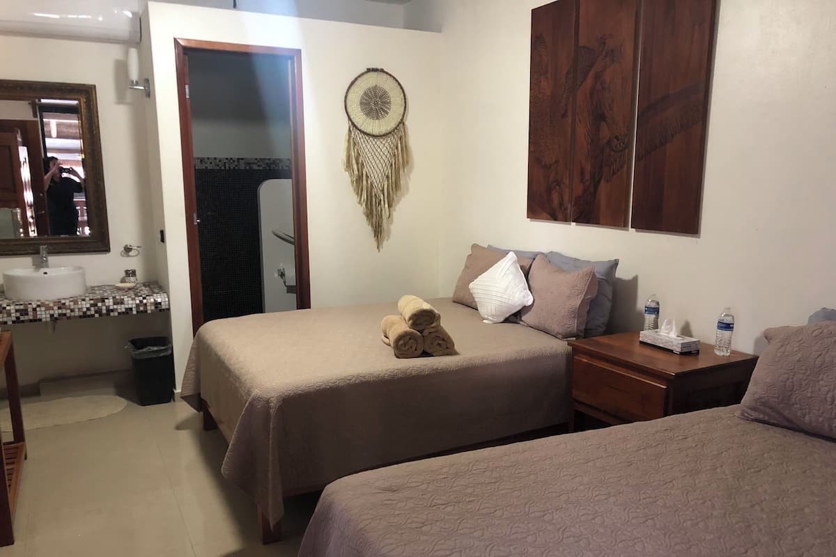 A hotel room with a bed, a bedside table, a nightstand, a mirror, a sink, and a dreamcatcher on the wall.