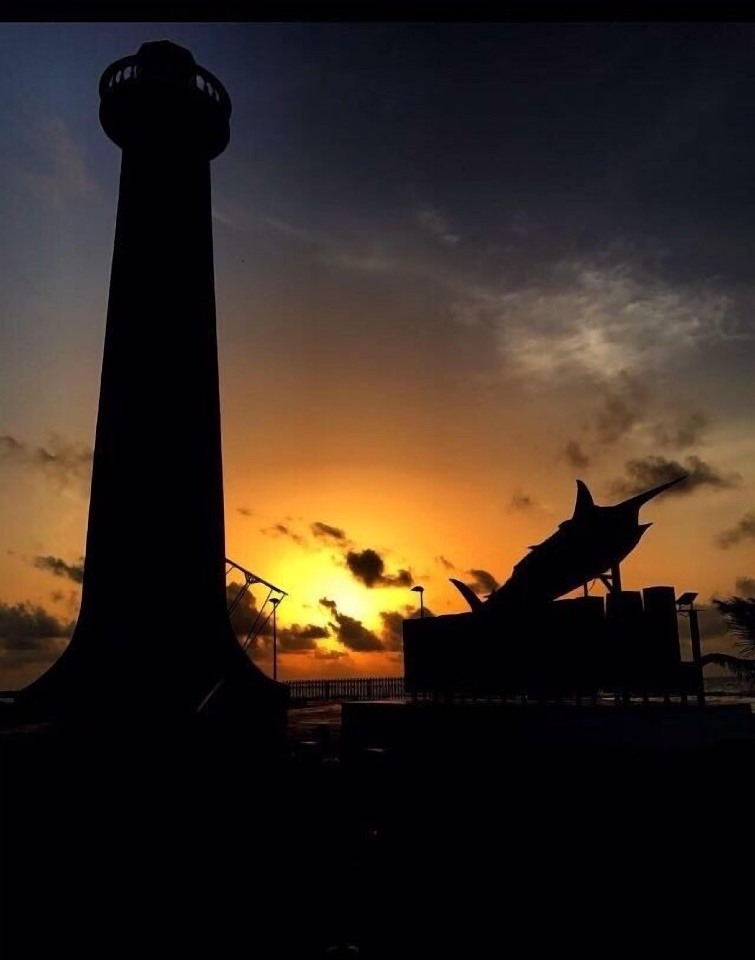 Eine Leuchtturmsilhouette vor einem Sonnenuntergangshimmel.