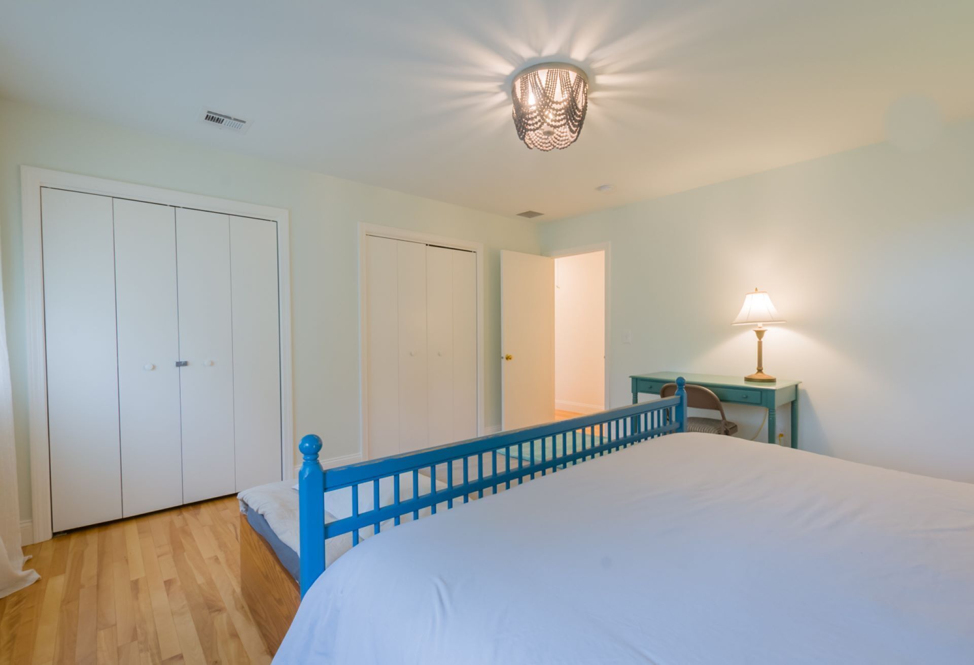 A bedroom with a bed, a desk, a chair, and a lamp.