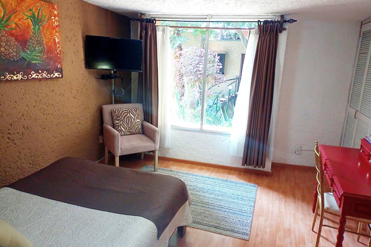 Una habitación de hotel con cama, sillón, televisión y una mesa de comedor.