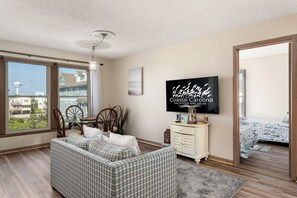 A living room with a large window, a sofa, a TV, and a view of the ocean. - Carolina Ocean Views: Dog Friendly, Ocean Views (Kill Devil Hills)